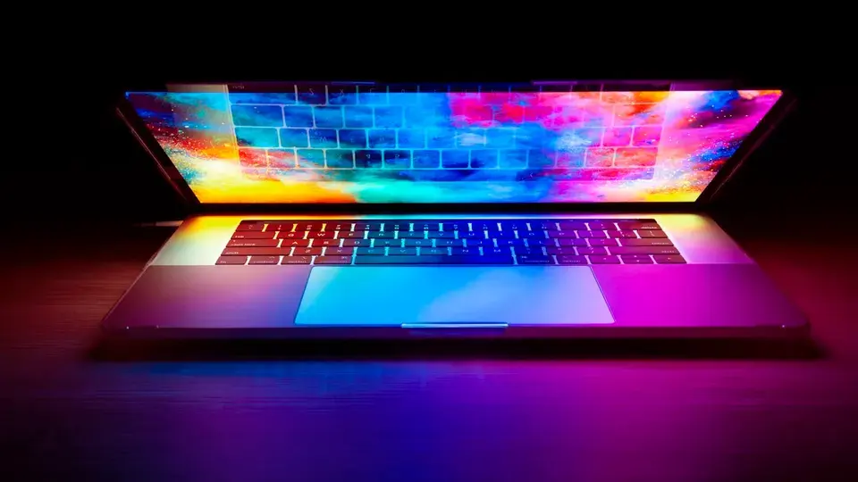 A half-open laptop with a glowing multicoloured screen on a dark desk