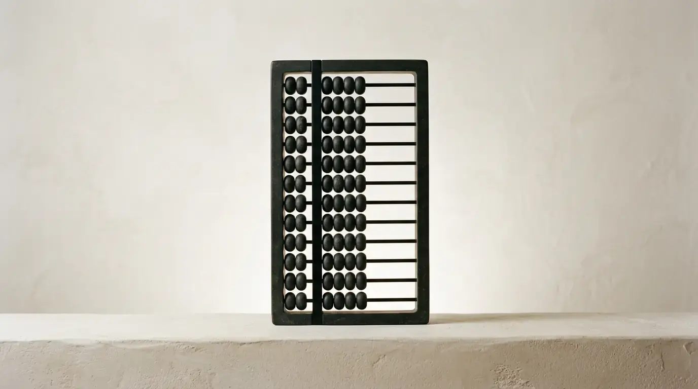 A black wooden abacus standing upright against a bare plaster wall in raking sunlight.