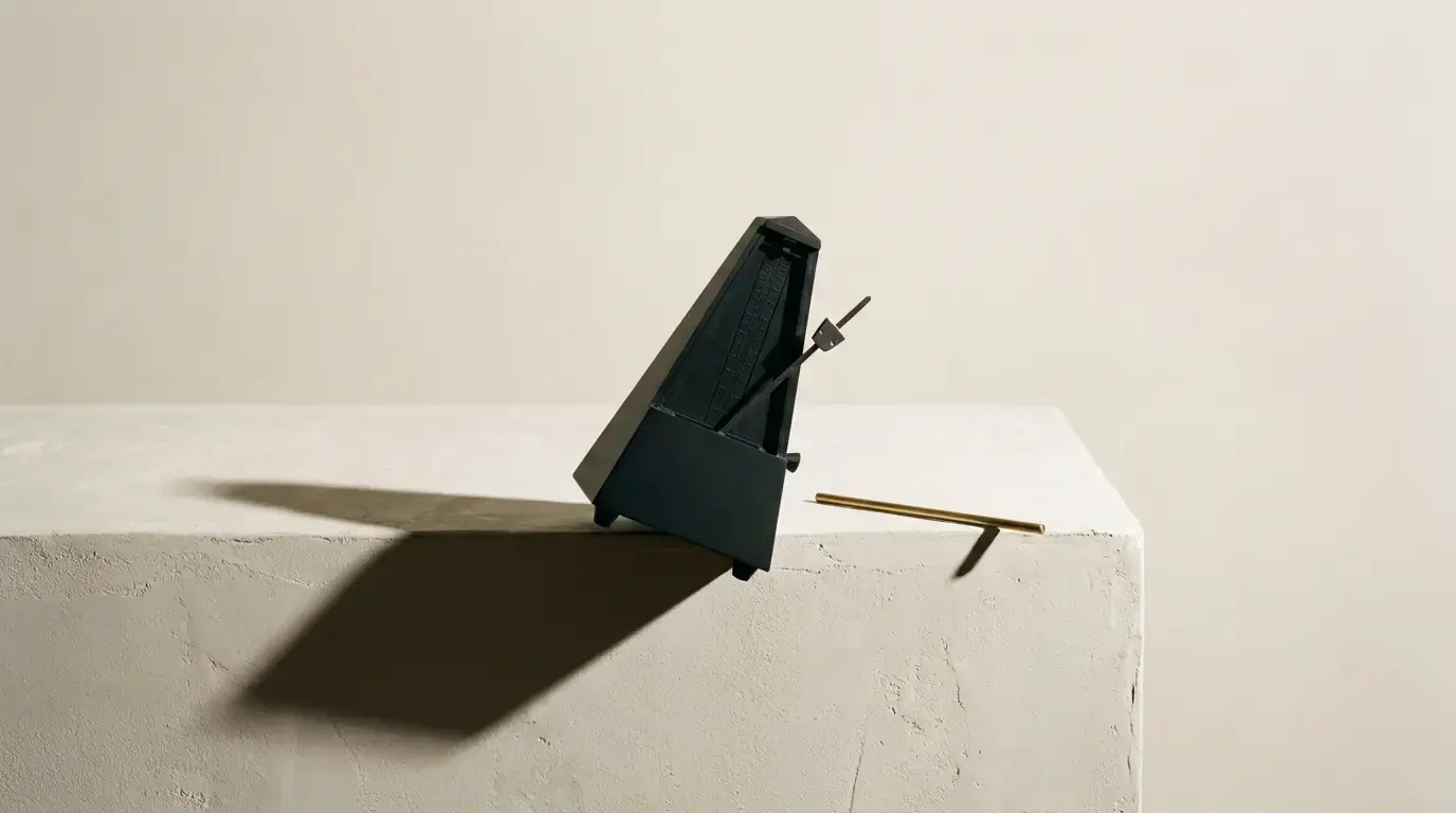 A black metronome with its pendulum stopped, standing at the edge of a plaster ledge