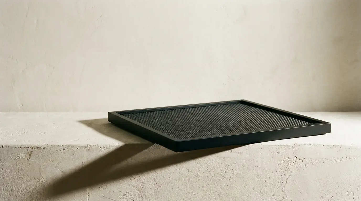 A shallow black tray with a fine mesh floor, jutting out over the edge of a plaster ledge
