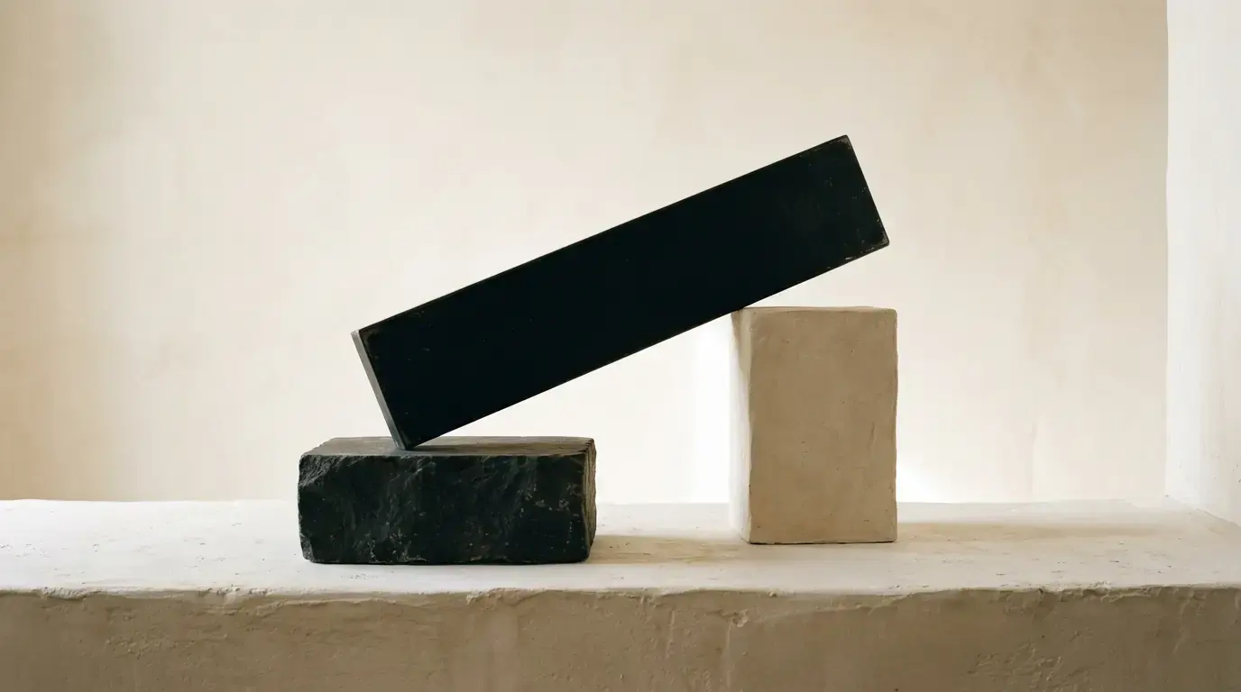 A long black slab balanced at an angle on a stone block, a pale plaster cube beside it.