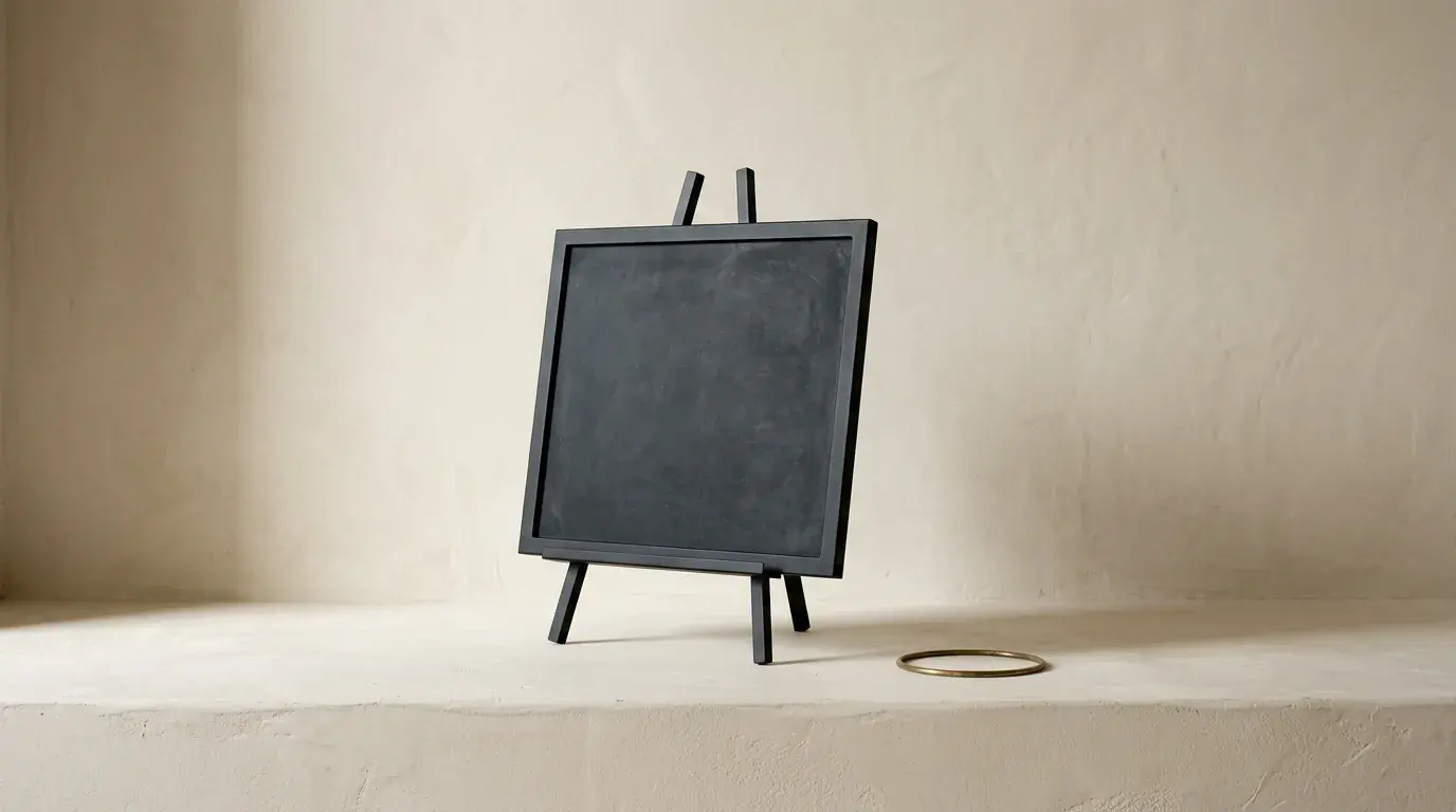 A blank dark slate standing on a small wooden easel on a plaster ledge, a thin brass ring lying flat nearby