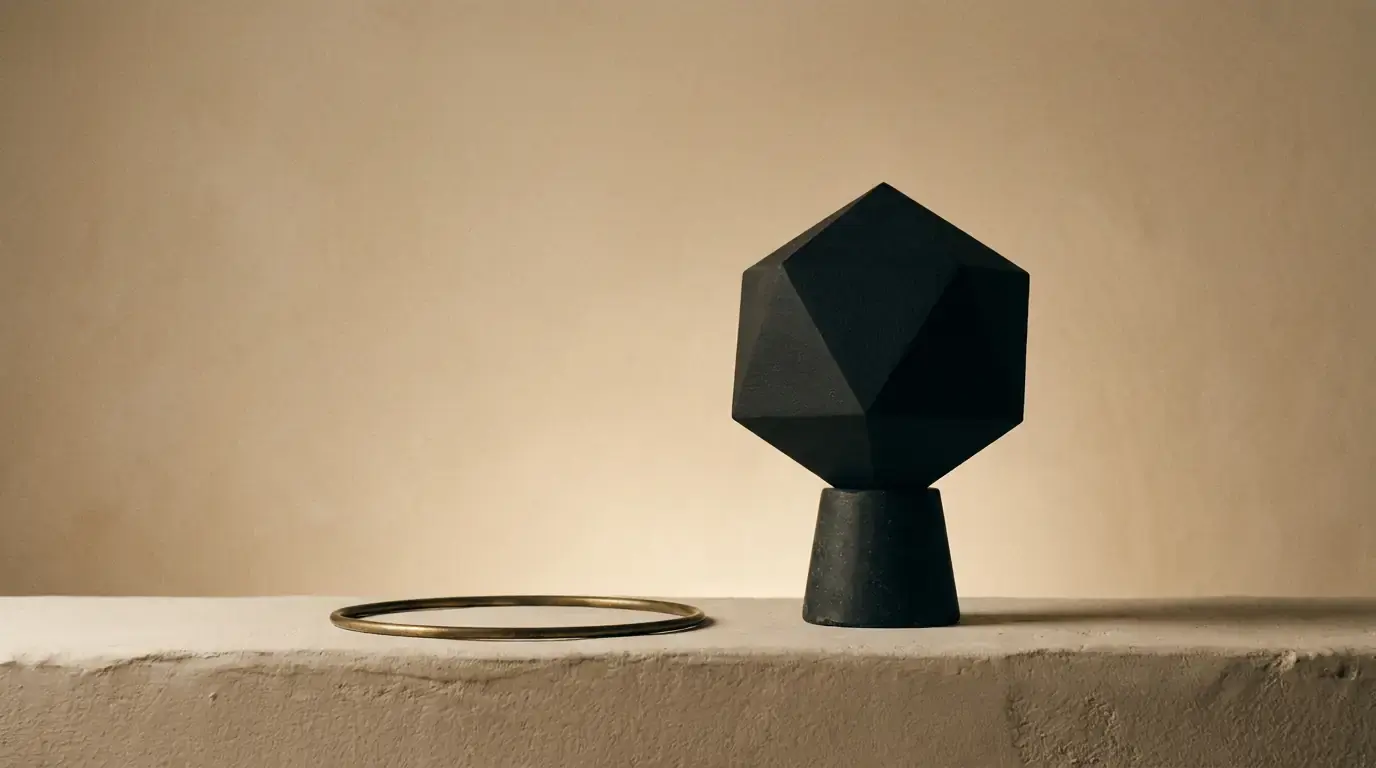A black faceted icosahedron on a tapered stone foot, a brass hoop lying on the ledge beside it