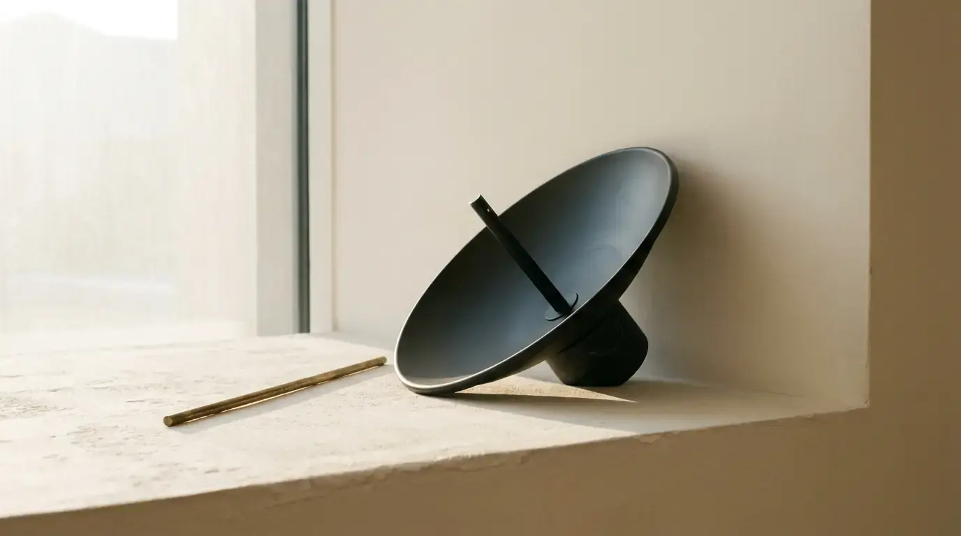 A black parabolic satellite dish tilted on a chalk-white plaster ledge, a thin brass rod beside it.